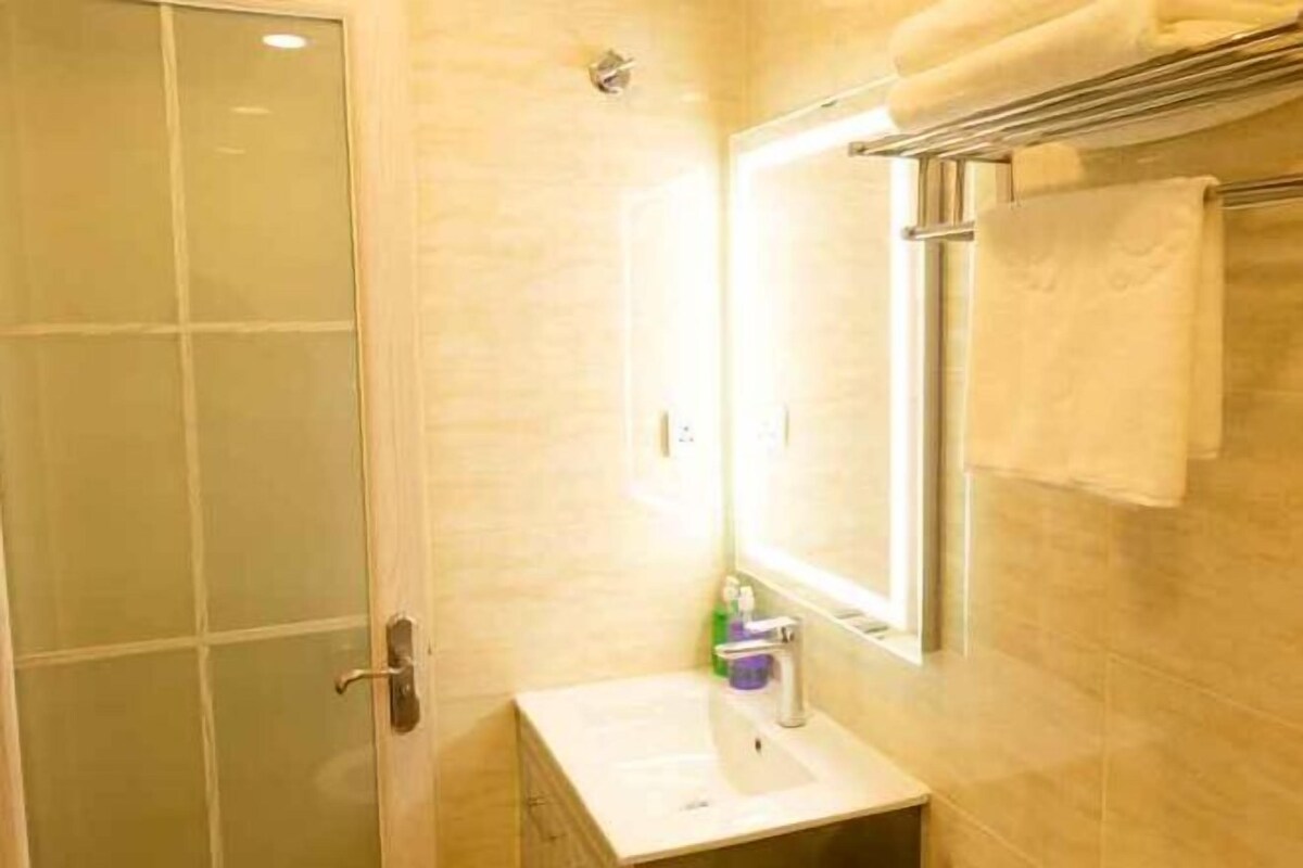 Un baño con mampara de vidrio, un lavamanos blanco y un perchero con toalla.