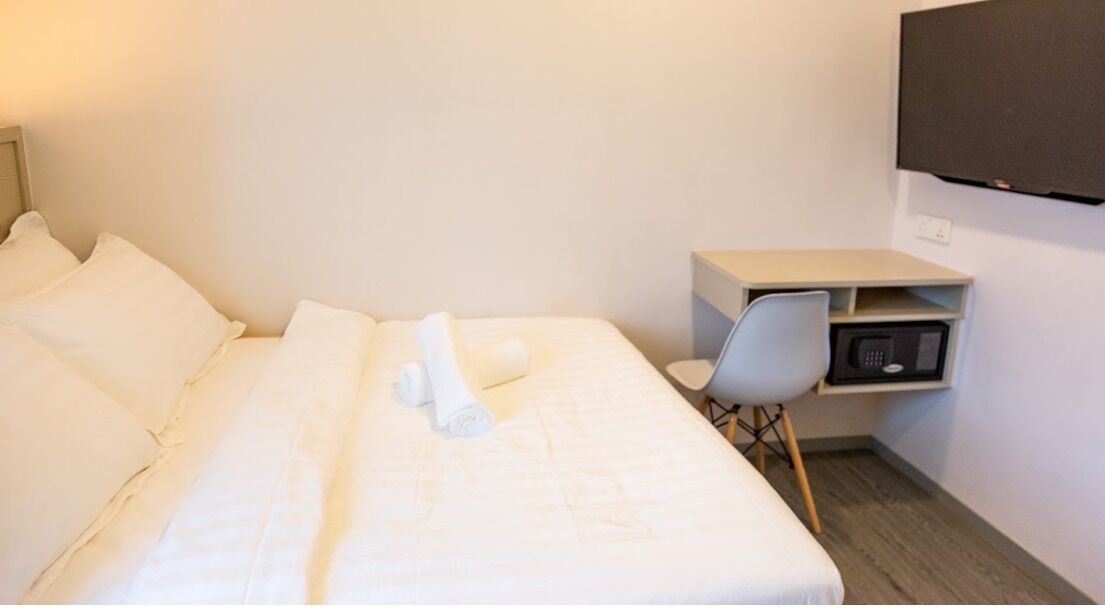A hotel room with a neatly made bed, a small desk with a chair, and a television mounted on the wall.
