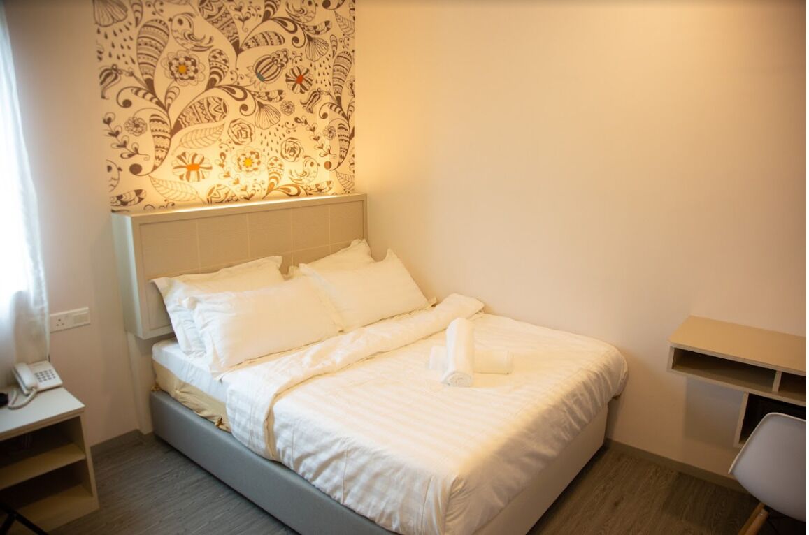 A neatly made bed with white linens and pillows, a bedside table with a telephone, and a patterned wall hanging above the bed.