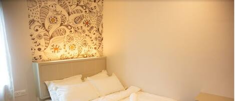 A neatly made bed with white linens and pillows, a bedside table with a telephone, and a patterned wall hanging above the bed.