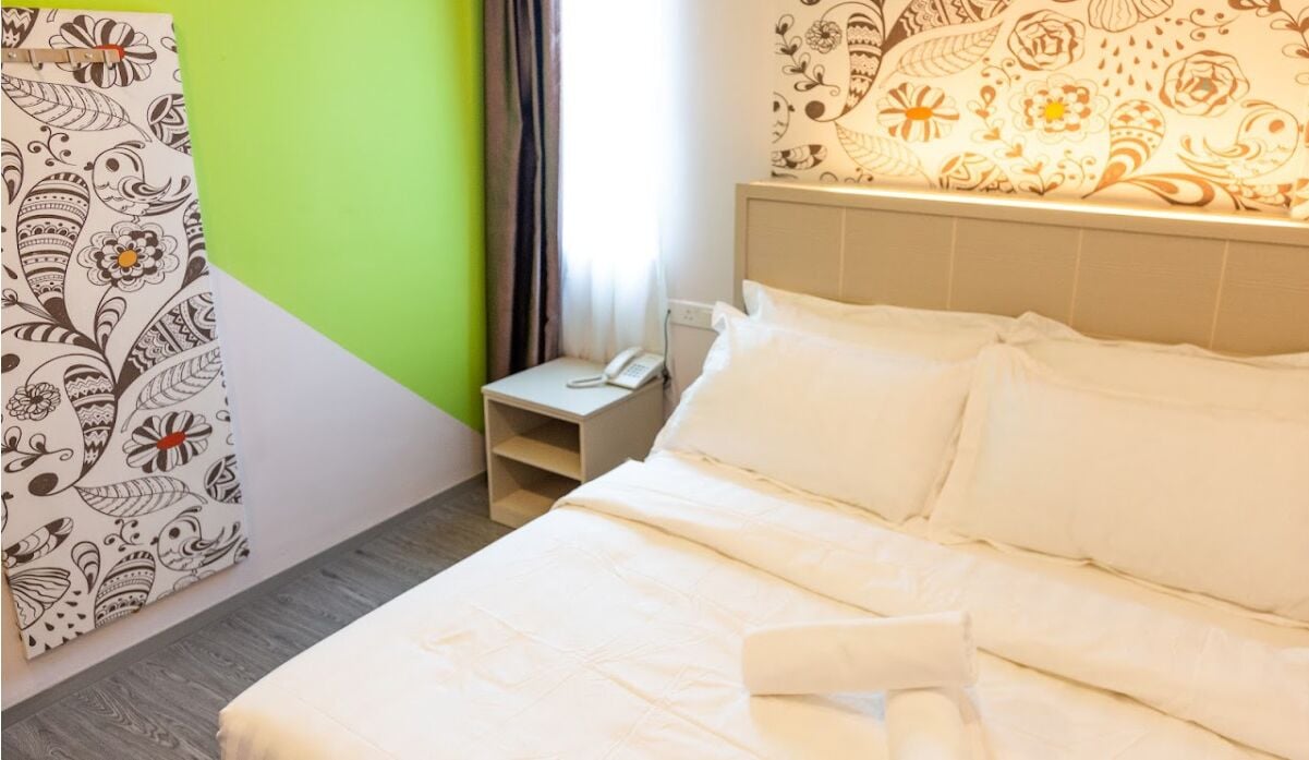 A hotel room with a bed, a bedside table with a phone, and a wall with a floral pattern.