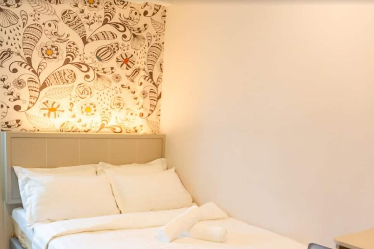 Ein ordentlich bezogenes Bett mit weißen Leinen und Kissen, einem Kopfteil und einer Wand mit einem gemusterten Wandteppich.