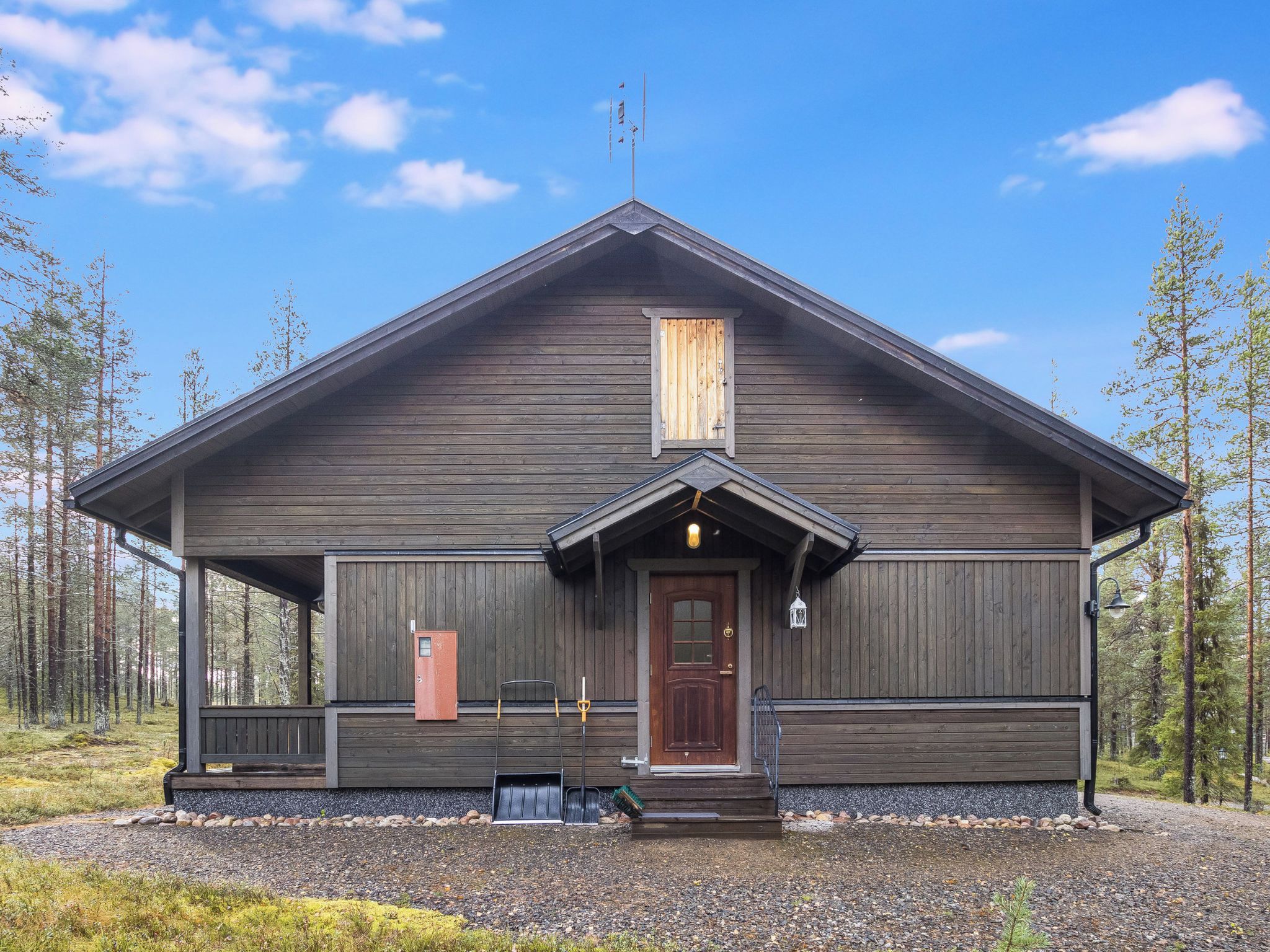 Puuinen mökki, jossa on kuisti, postilaatikko ja ikkunalla varustettu ovi.