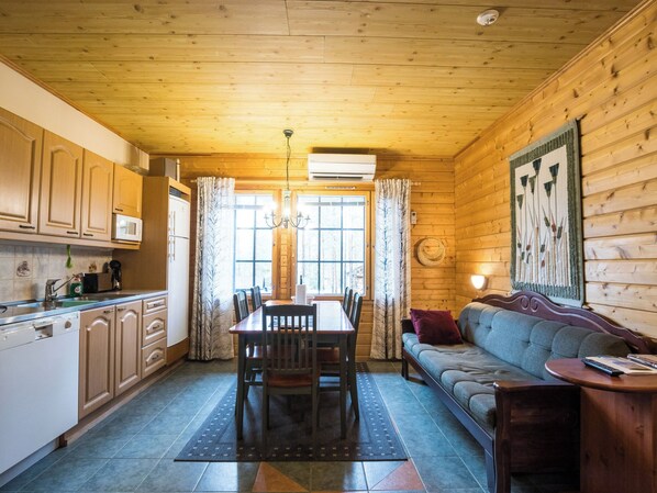 Un intérieur en bois comprenant une table à manger, des chaises, un canapé et un coin cuisine avec des placards et des appareils électroménagers.