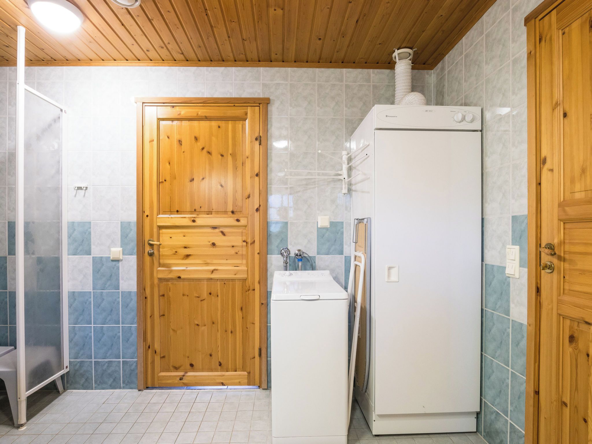 A bathroom with a wooden door, a white washing machine, and a tiled floor.