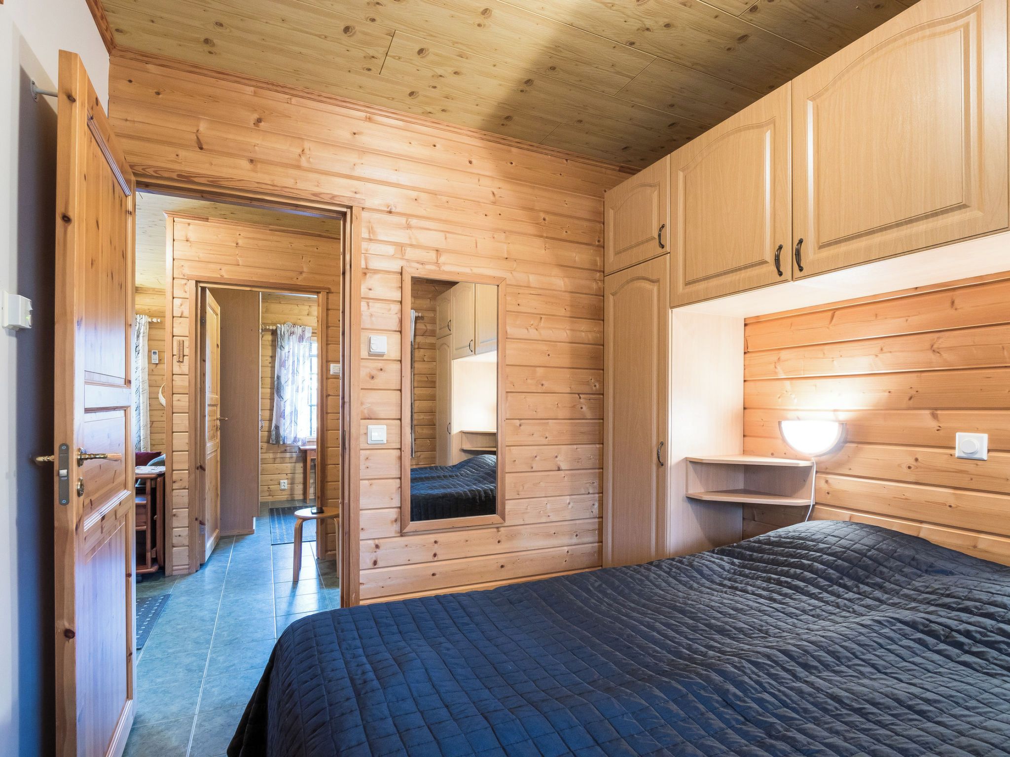 A wooden cabin interior with a bed, a mirror, and a small table.