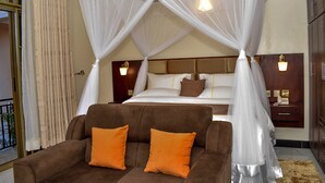 Une chambre à coucher avec un lit à baldaquin, un canapé marron agrémenté de coussins orange et une table de chevet avec une lampe.
