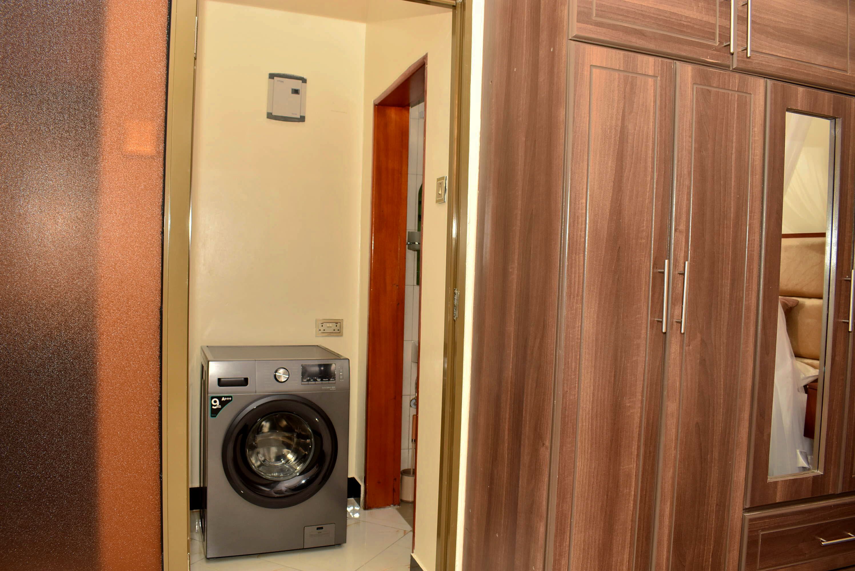 Une buanderie équipée d’un lave-linge, d’une armoire en bois et d’un miroir qui reflète un lit.