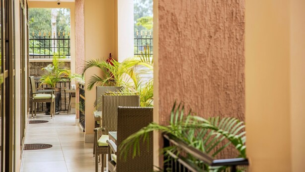 Un couloir meublé de mobilier en osier et agrémenté de plantes en pot, qui mène à un balcon offrant une vue sur la verdure.