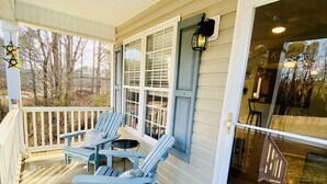 A covered porch with two Adirondack chairs, a small table, and a glass door leading to an outdoor area. - **cozy country** *stargazing acre* (Franklinton)