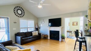A spacious living room with a fireplace, a black leather sofa, a dining area with a table and chairs, and a ceiling fan. - **cozy country** *stargazing acre* (Franklinton)