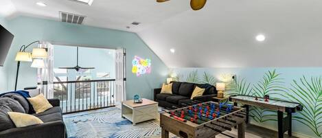 A cozy living room with a foosball table, a sofa, a coffee table, and a ceiling fan.