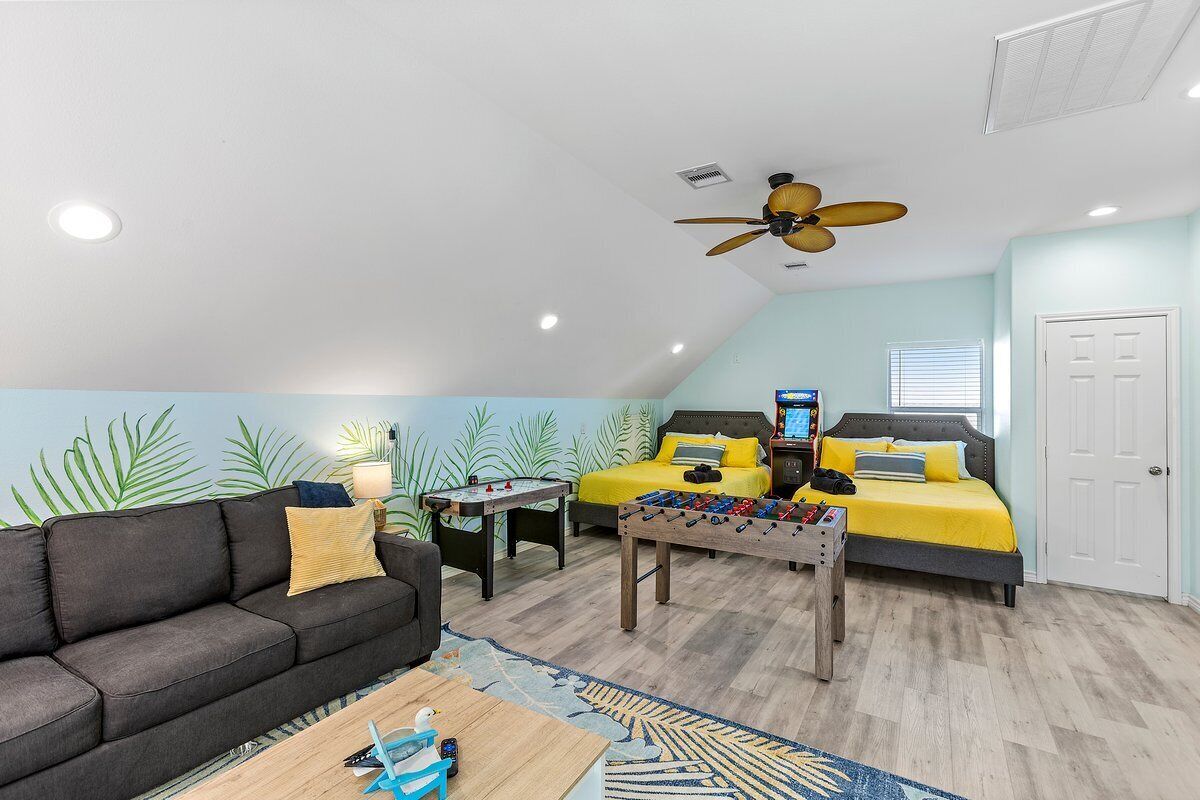 A cozy room with a sofa, a bed with yellow bedding, a foosball table, and a ceiling fan.