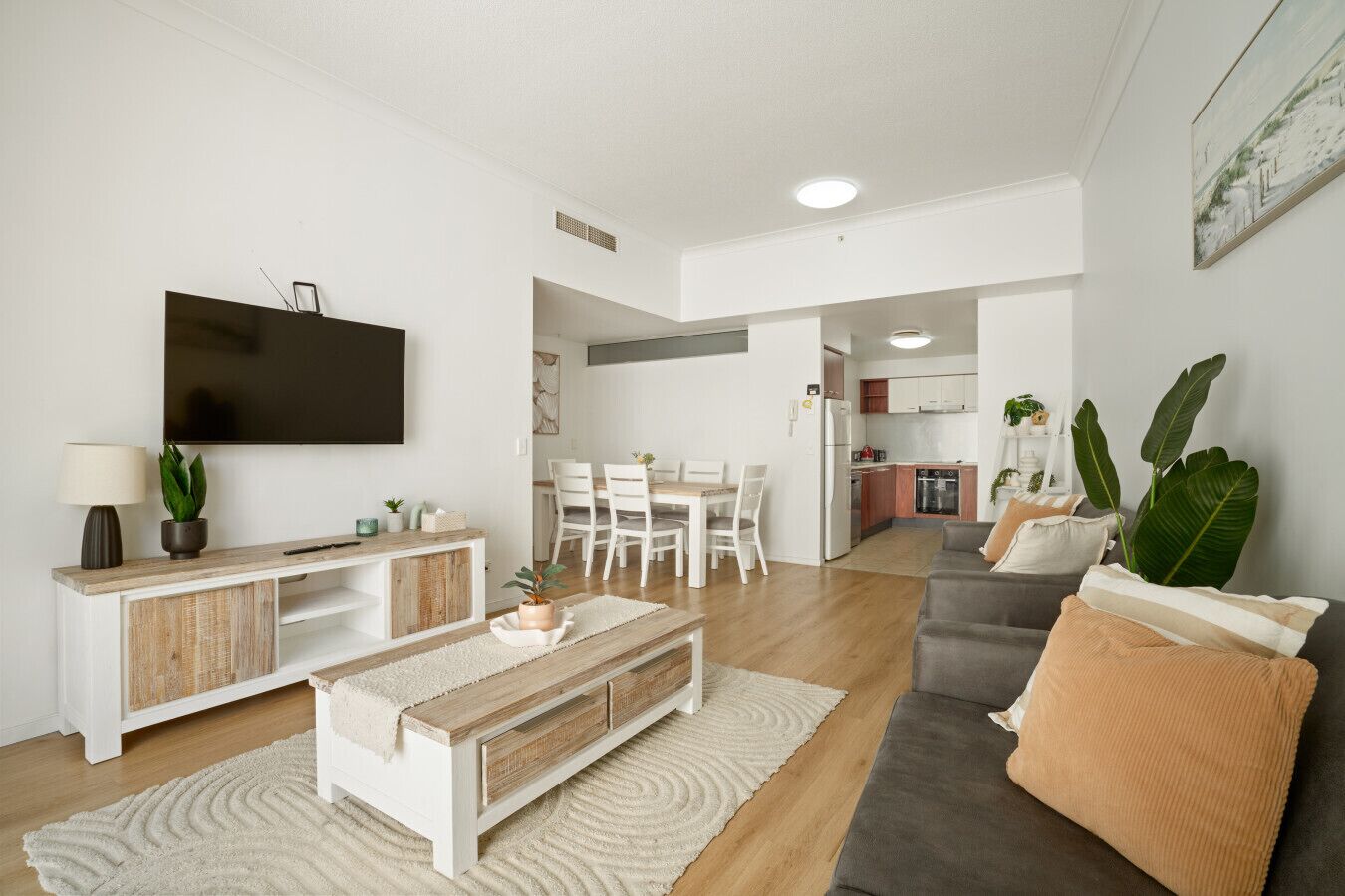 Un salon moderne avec un téléviseur à écran plat, une console en bois, un canapé gris et un coin repas à l’arrière-plan.