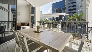A balcony with a wooden table, white chairs, and a potted plant. - Surfers Paradise Getaway: Amazing Resort Amenities (Surfers Paradise)