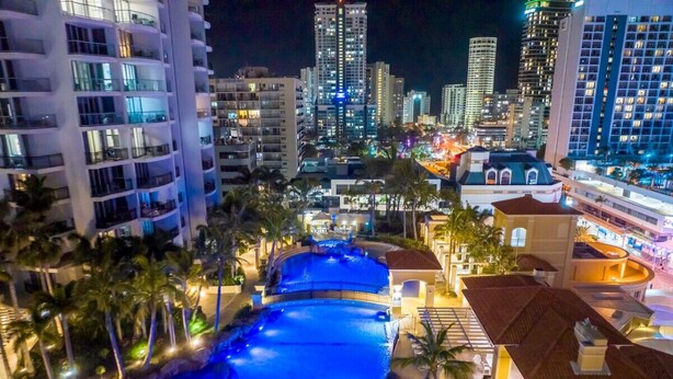 A large swimming pool with a waterfall feature, surrounded by palm trees and modern buildings. - Surfers Paradise Getaway: Amazing Resort Amenities (Surfers Paradise)