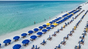 Ein Strand mit Reihen von blauen und gelben Sonnenschirmen und Liegestühlen.