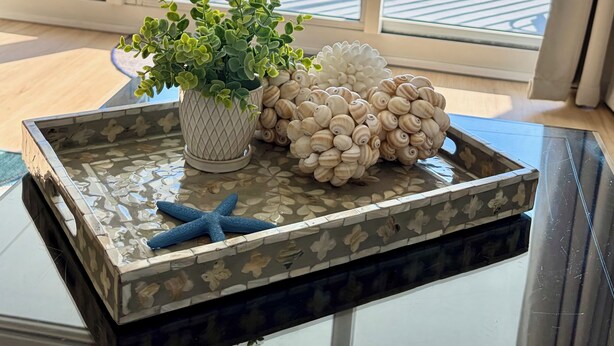 Ein Balkon mit Blick auf das Meer, ein Blumentopf und dekorative Muscheln auf einer Tablett.