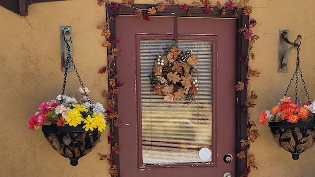 Uma porta marrom adornada com uma grinalda, dois cestos de flores pendurados e um pequeno candeeiro.