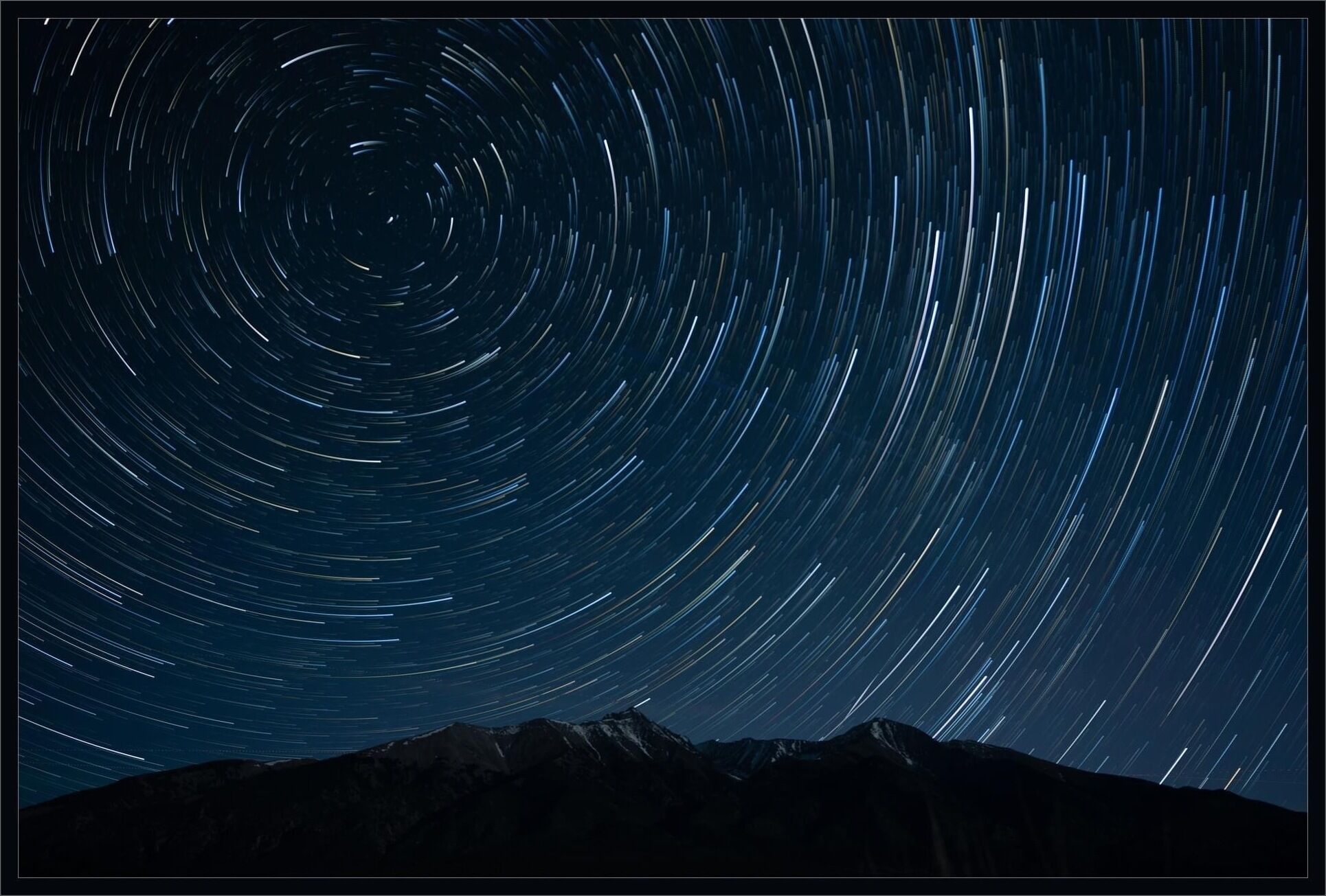 A star trail photograph with a mountain silhouette at the bottom.