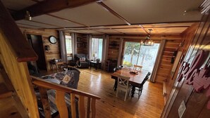Een chaletinterieur met een houten eettafel, stoelen, een bank en een trap.