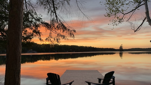 Een houten steiger met twee stoelen, gericht op een rustig meer bij zonsondergang.