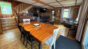 Een ruime woonkamer met een houten eettafel, stoelen, een bank en een open haard.