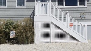 Una casa sulla spiaggia con una scala bianca che conduce a un portico coperto, un piccolo ponte e vista sull'oceano.