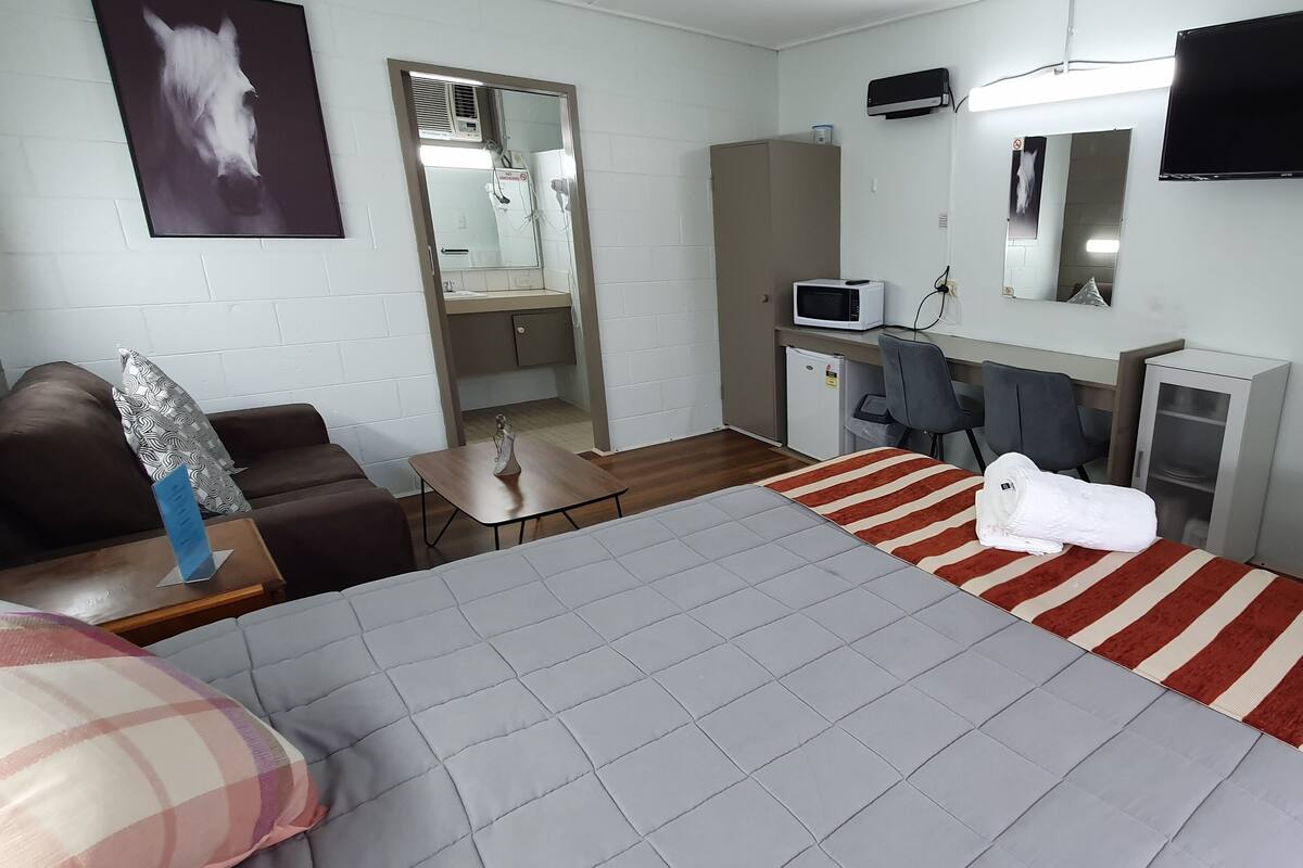Ein Hotelzimmer mit einem großen Bett, einem Schreibtisch, einem Stuhl, einem Fernseher und einem sichtbaren Badezimmer hinter einer offenen Tür.