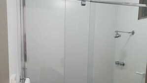 A glass-enclosed shower stall with a blue-tiled floor, a towel rack, and a showerhead. - Morwell Parkside Motel (Morwell)