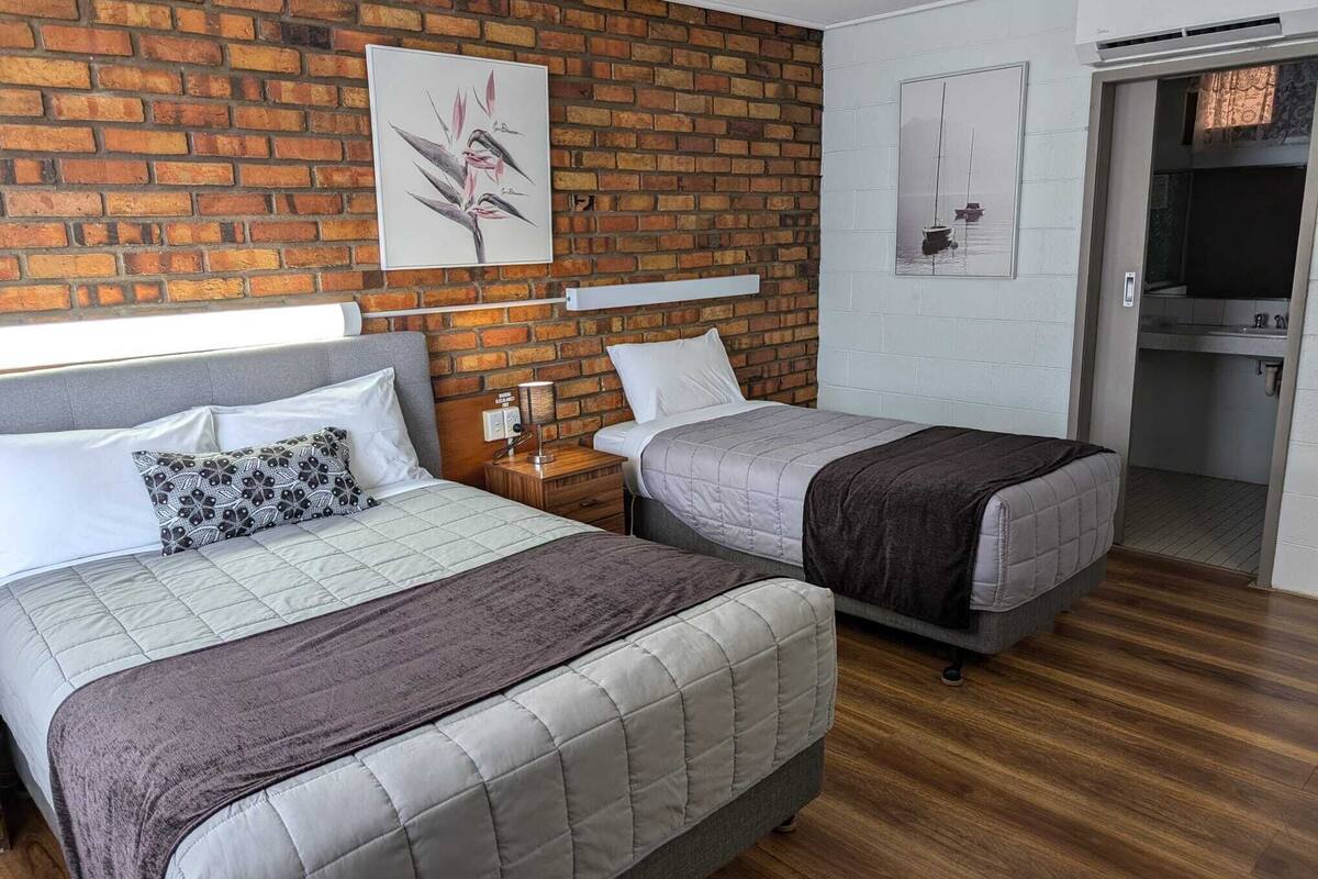 Ein Zimmer mit zwei Betten, einer Ziegelwand und einem Gemälde eines Bootes.