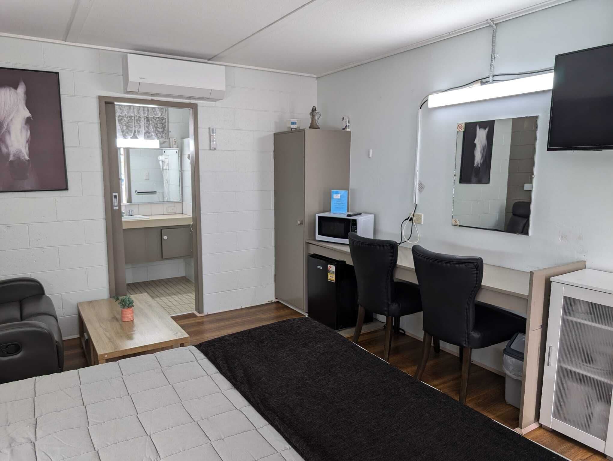 A compact room with a bed, a desk, a chair, a microwave, and a TV.