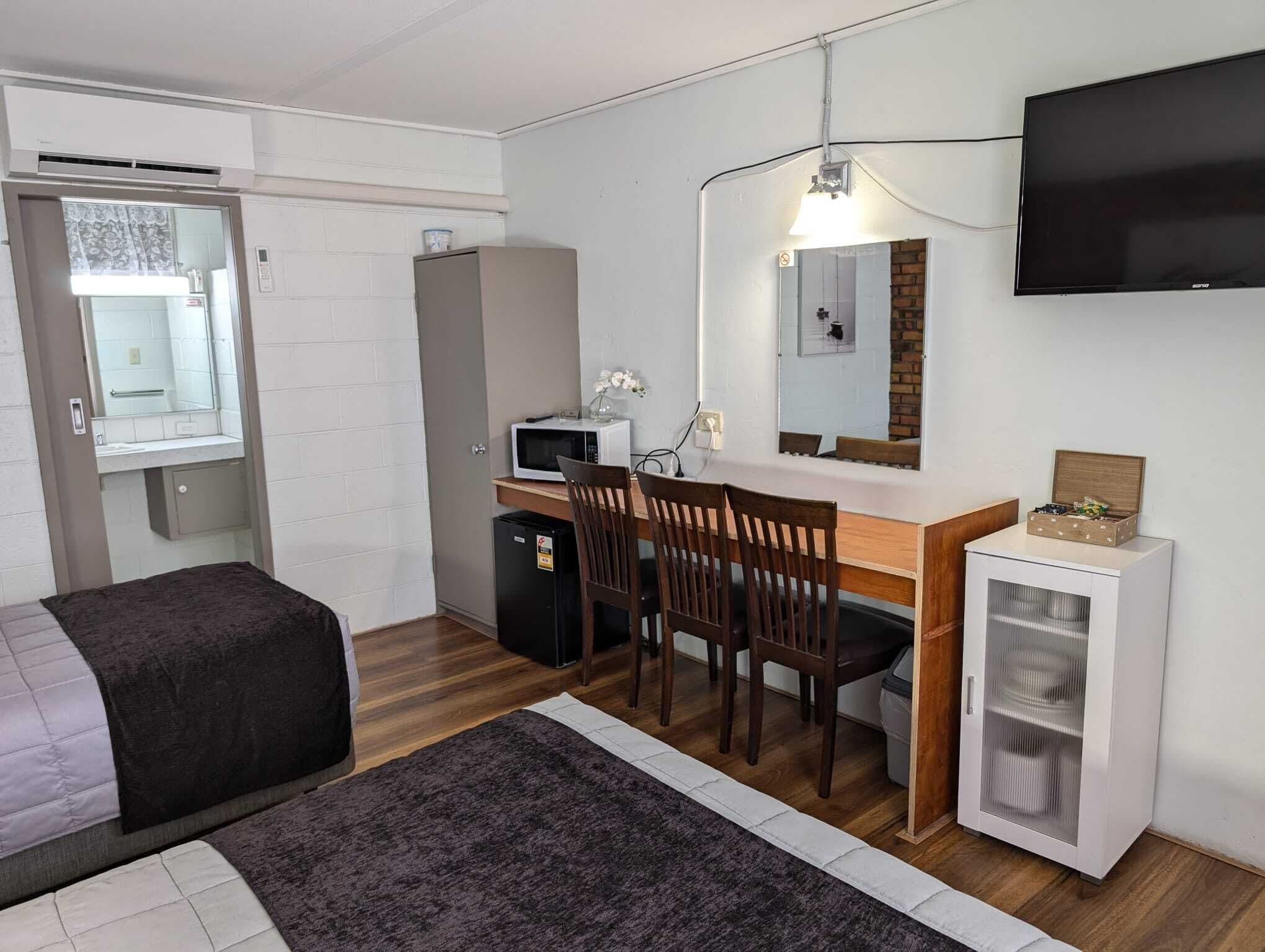 Habitación pequeña con cama, escritorio con silla, microondas, refrigerador compacto, televisor y armario.