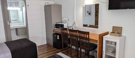 Habitación pequeña con cama, escritorio con silla, microondas, refrigerador compacto, televisor y armario.