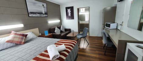 Quarto de hotel com cama, escrivaninha, cadeira, televisão e banheiro visível por uma porta aberta.