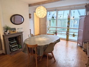 A dining area with a round table, chairs, a fireplace, and a view through large windows. - The Courtgain Catamaran (Saint-Valery-sur-Somme)