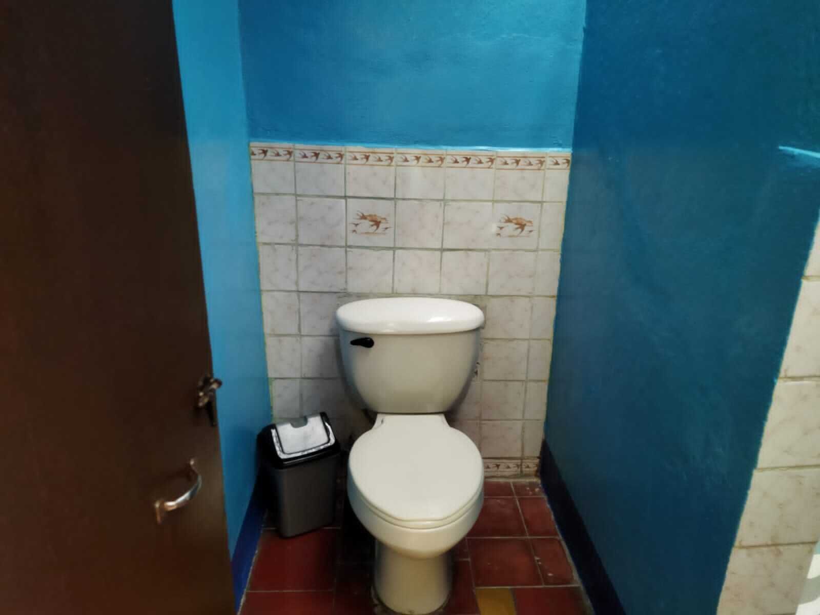 Un baño pequeño con un inodoro, un cubo de basura y una puerta.