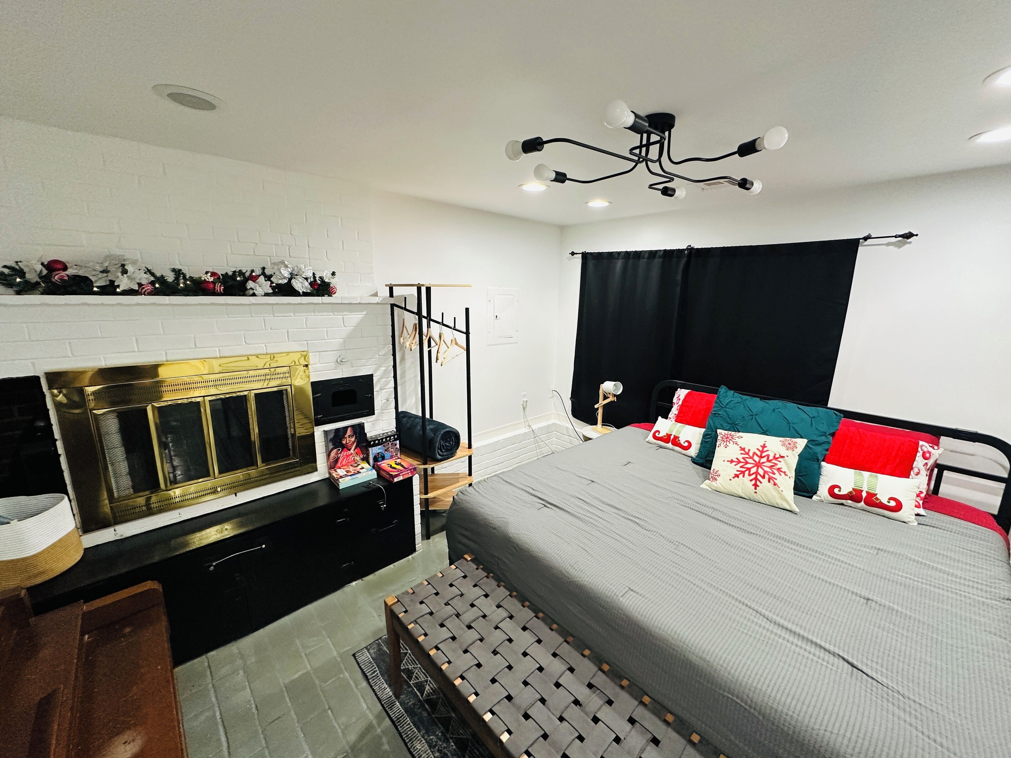 A bedroom with a bed, a black and white striped rug, a white brick wall, a fireplace, and a ceiling light fixture.