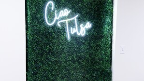 Ett rum med en grön, strukturerad bakgrund och en neonreklamskylt med texten ”Ciao Tutto”.