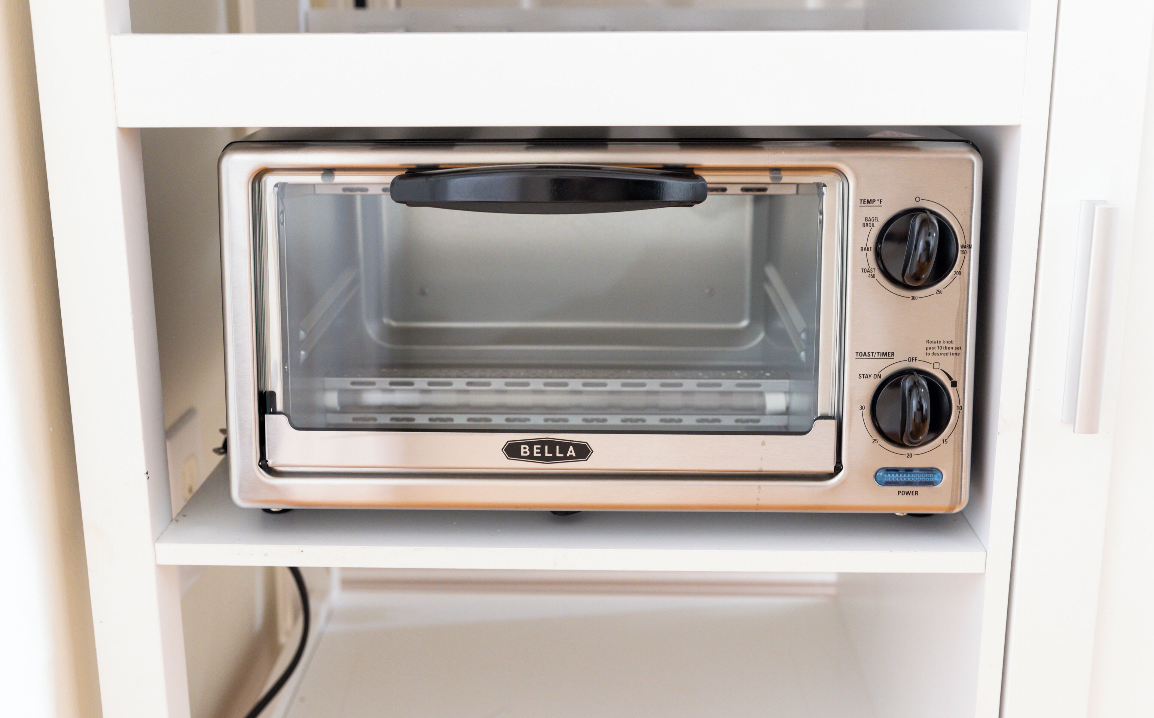 Un forno tostatutto compatto con pannello di controllo, che include regolazioni di temperatura e timer, inserito in un mobile bianco.