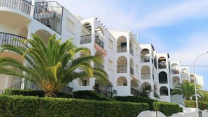A multi-story building with balconies, white walls, and palm trees.