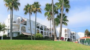 A multi-story hotel with balconies, palm trees, and a well-maintained lawn.