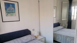 A hotel room with two beds, a nightstand, a lamp, a framed picture on the wall, and a mirror.