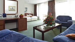 Ein Hotelzimmer mit einem Bett, einem Schreibtisch, einem blauen Sofa, einem Couchtisch und einem großen Fenster mit Vorhängen.