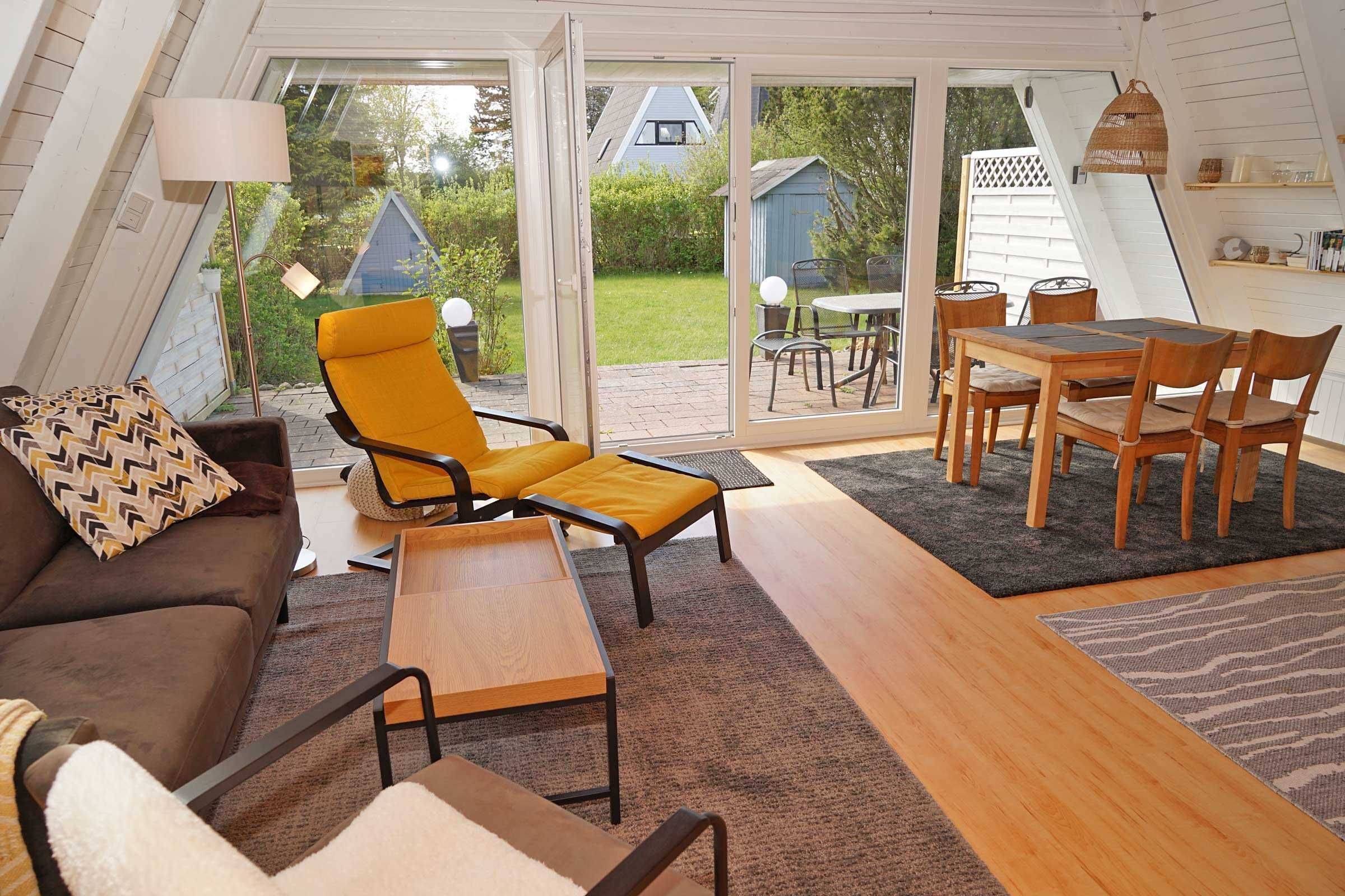 A cozy living room with a sofa, a yellow armchair, a wooden table, and a dining set.