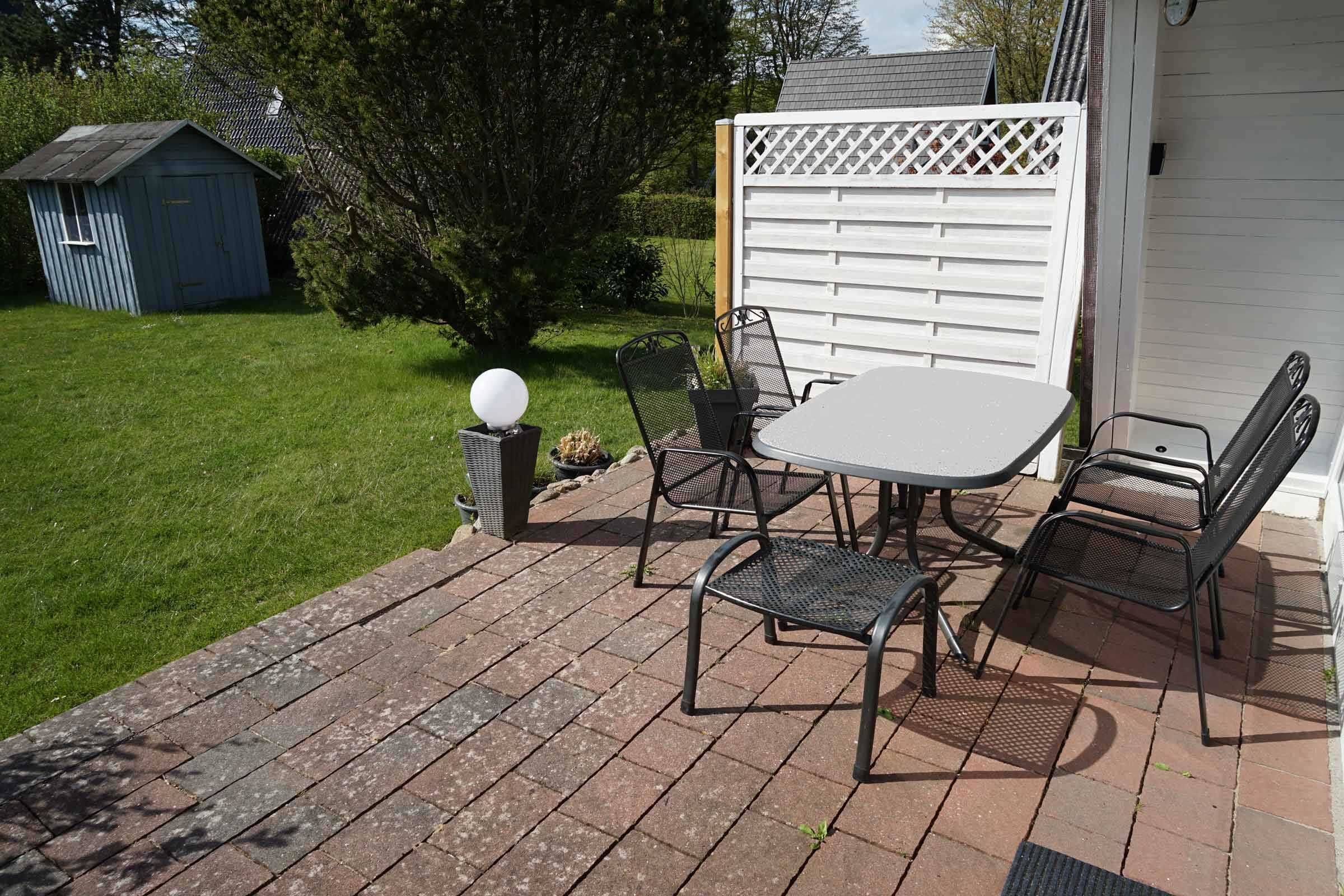 A patio with a table and chairs, a small shed, and a white fence.