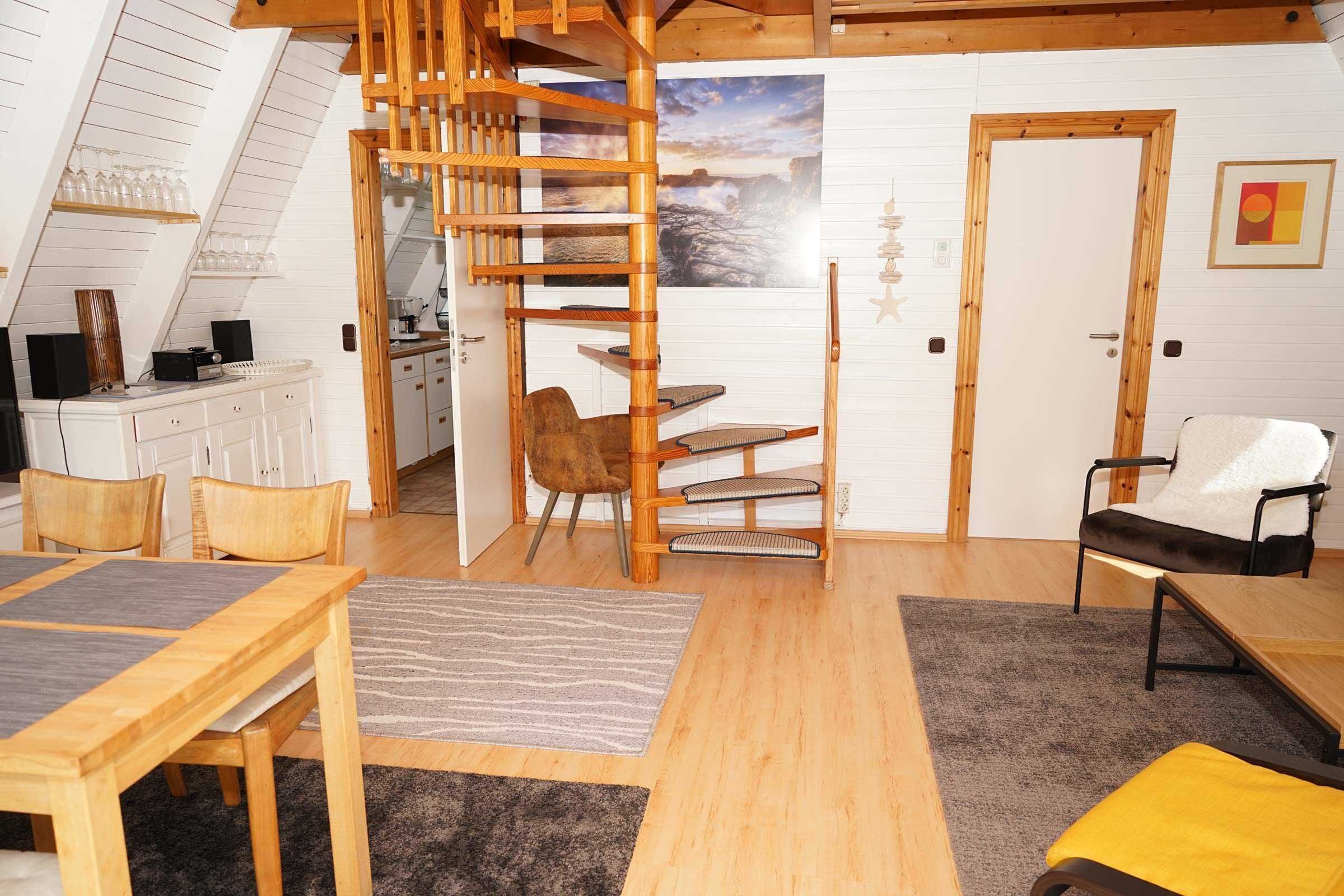 A cozy loft bedroom with a wooden staircase, a dining area, and a view of the sea.
