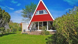Una casa triangular de color rojo y blanco con un patio y un pequeño jardín.