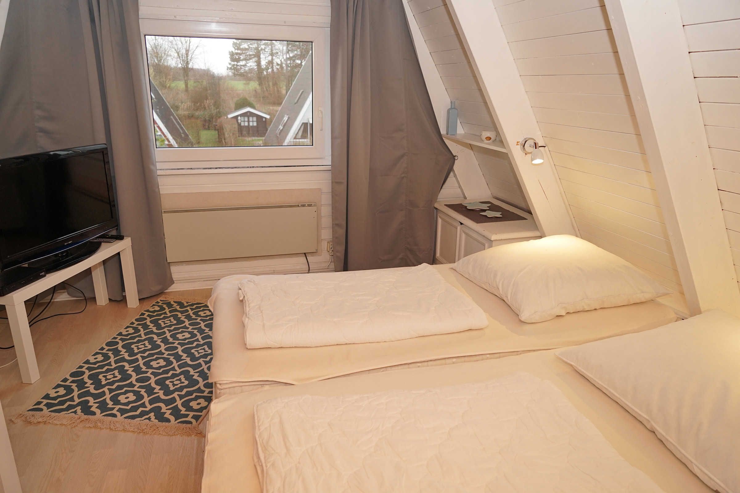 A bedroom with two beds, a TV, and a window with curtains.