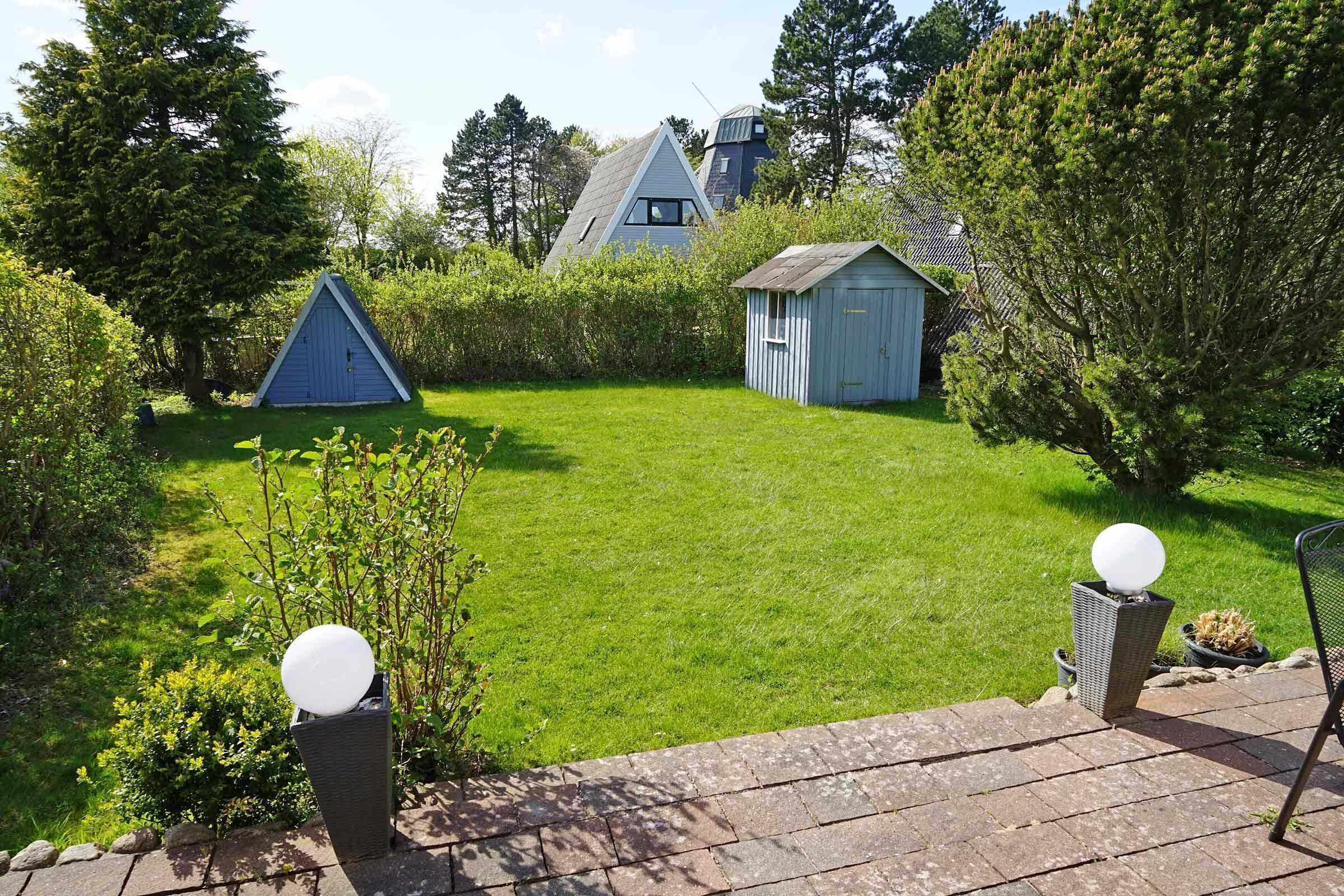 A well-maintained garden with a lawn, a small shed, and a triangular structure.